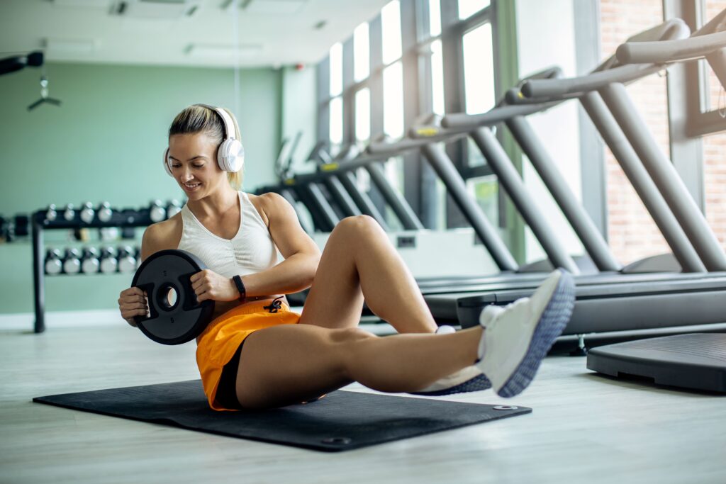 young athletic woman exercising situps with weight plate gym